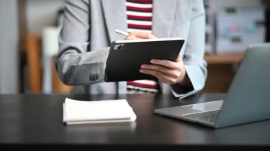 Mutlu Asyalı iş kadını ofiste dizüstü bilgisayar ve tablet bilgisayar kullanarak not alıyor. 