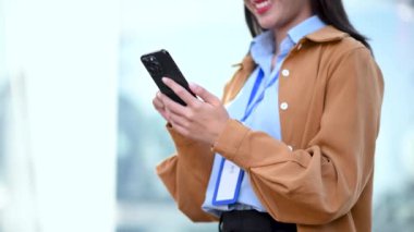 Şehir caddesinde cep telefonuyla çalışan mutlu Asyalı iş kadını.