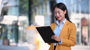 Asyalı mutlu iş kadını şehir sokaklarında not tutuyor.