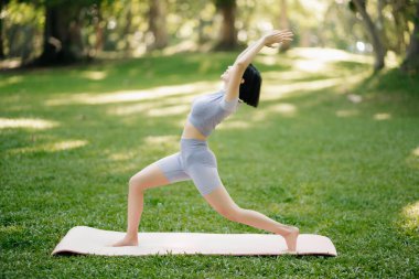 Yaz parkında yoga yapan genç bir kadının portresi, bulanık ağaçlar. Sağlıklı yaşam tarzı ve rahatlama kavramı