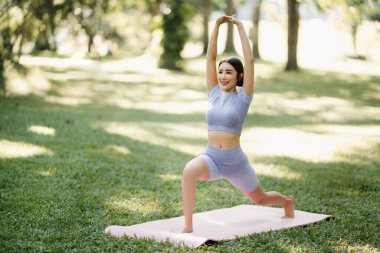 Yaz parkında yoga yapan genç bir kadının portresi, bulanık ağaçlar. Sağlıklı yaşam tarzı ve rahatlama kavramı