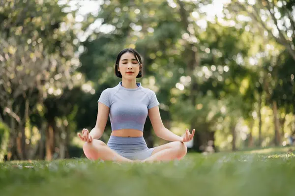 Asian young woman meditating sitting in lotus pose in summer garden. Inner peace and mindfulness concept