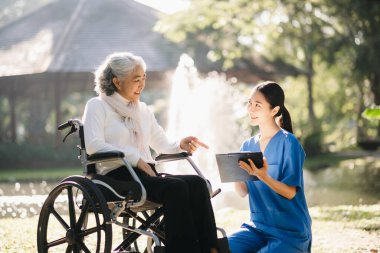 Asyalı yaşlı, yaşlı, yaşlı, tekerlekli sandalyede, Asyalı, dikkatli bir bakıcı ve bahçede hastaları cesaretlendiren bir kadın. Bakıcının ve kıdemli sağlık sigortasının dikkatine.