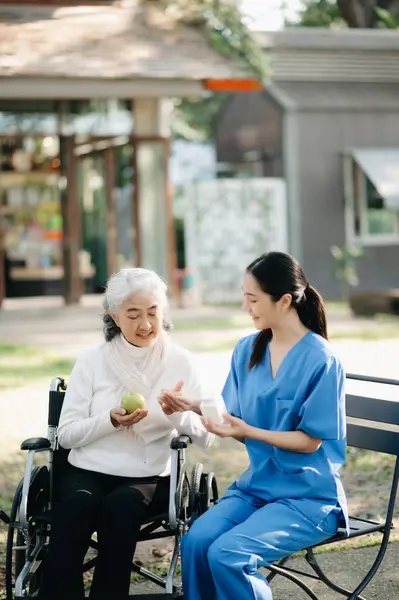 Elderly asian senior woman on wheelchair with Asian careful caregiver and encourage patient in garden. with care from a caregiver and senior health insurance