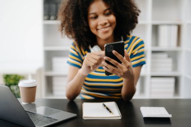 Afrikalı Amerikalı kız öğrenci, akıllı telefon ve dizüstü bilgisayar kullanarak kulaklık takıyor. 