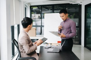 Nazik yönetici yönetici iş çözümlerini paylaşıp tartışır ve modern ofiste Asyalı erkek pazarlama yöneticisiyle tablet ve dizüstü bilgisayarda fikirler planlar