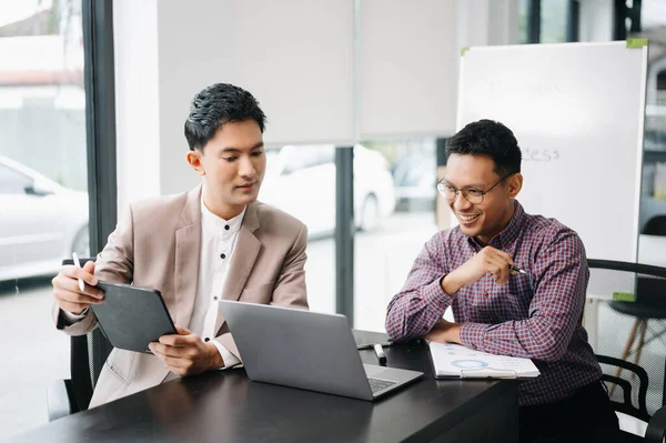 Kind leader executive manager share and discuss business solutions plan ideas on tablet and laptop with Asian male marketing manager in modern office