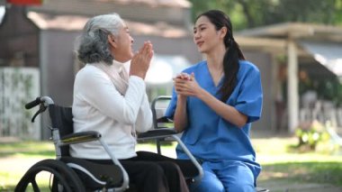 Genç Asyalı hemşire hastane parkında tekerlekli sandalyedeki yaşlı kadınla konuşuyor. Kıdemli sağlık hizmeti kavramı