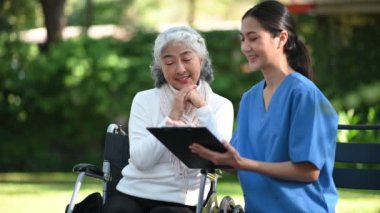 Asyalı doktor hastane parkında yaşlı bir kadını muayene ederken not alıyor.