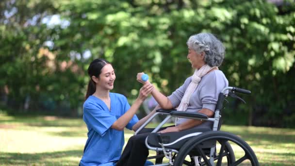 年轻的亚洲女医生帮助一位坐轮椅的老年妇女在医院公园用哑铃进行锻炼 高级保健概念 — 图库视频影像