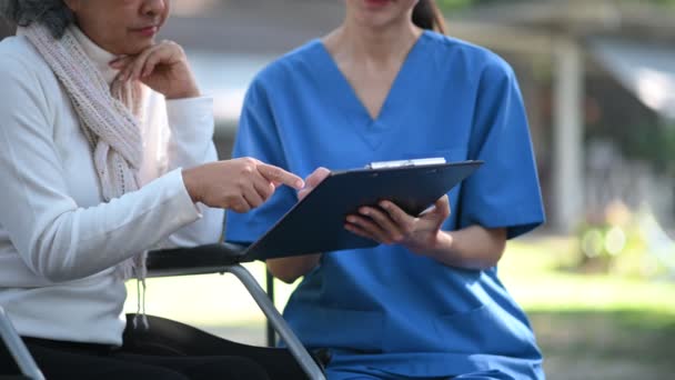 亚洲医生在医院公园检查坐轮椅的亚洲老年妇女病人时做笔记 — 图库视频影像