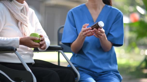 年轻的亚洲护士在医院公园给坐在轮椅上的老年妇女吃药 高级保健概念 — 图库视频影像