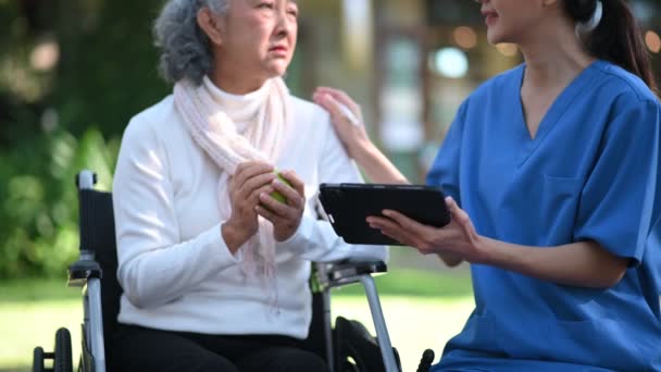Ασιάτης Γιατρός Κρατάει Σημειώσεις Ενώ Εξετάζει Ηλικιωμένη Ασιάτισσα Ασθενή Αναπηρικό — Αρχείο Βίντεο