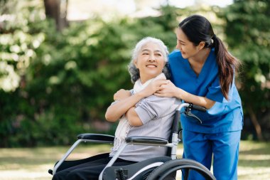 Asyalı yaşlı, yaşlı, yaşlı, tekerlekli sandalyede, Asyalı, dikkatli bir bakıcı ve bahçede hastaları teşvik eden bir kadın.
