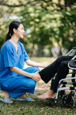 Asyalı fizyoterapist bahçede yaşlı bir hastaya sırt ağrısı için yardım ediyor. Huzurevi hastane bahçesi konsepti.
