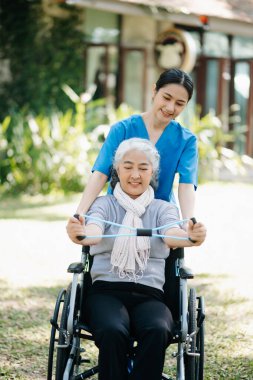 Asyalı fizyoterapist bahçede yaşlı bir hastaya sırt ağrısı için yardım ediyor. Huzurevi hastane bahçesi konsepti.