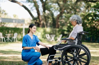 Asyalı fizyoterapist bahçede yaşlı bir hastaya sırt ağrısı için yardım ediyor. Huzurevi hastane bahçesi konsepti.