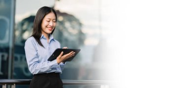 Genç Asyalı iş kadını arka planda iş merkezi olan büyük şehirde sokakta dijital tablet kullanıyor.