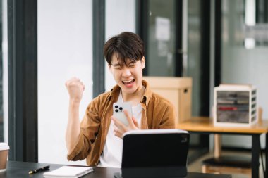 Asyalı işadamı, ofisteki akıllı telefon ve dijital tablet çalışmalarından memnun ve memnun.