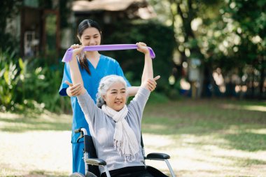 Asian physiotherapist helping elderly woman exercising in the garden