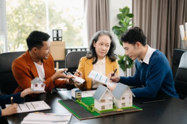 Emlak komisyoncusu ev modelini müşteriye sunuyor ve ofiste sigorta sözleşmesi imzalıyor.