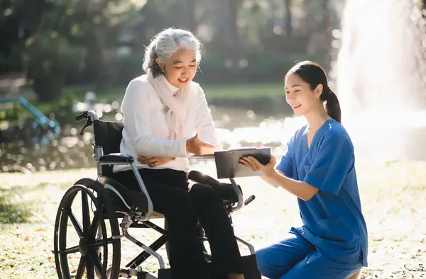 Elderly asian senior woman on wheelchair with Asian careful caregiver and encourage patient in garden. with care from a caregiver and senior health insurance