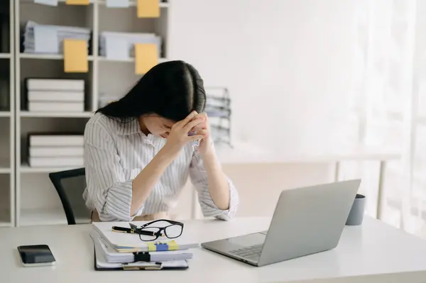 アジアの女性は片頭痛の頭の緊張を感じます オフィスでラップトップで作業しながら 過労のビジネス女性の金融 ストック写真