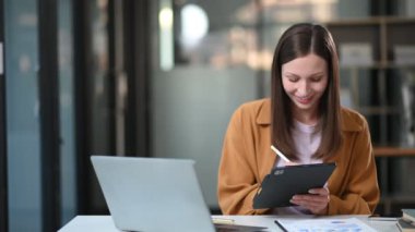 Modern ofisteki masada otururken dijital tablet ve laptop üzerinde çalışan genç ve güzel bir iş kadını.