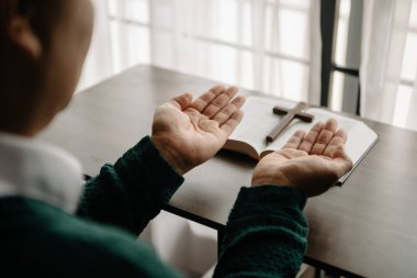 Yazıtları inceleyen bir adam. Ellerindeki tahta haç. Hıristiyan eğitimi kutsal yazıtların açılıp Tanrı 'ya dua etmesini sağlar.