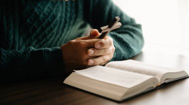 Yazıtları inceleyen bir adam. Ellerindeki tahta haç. Hıristiyan eğitimi kutsal yazıtların açılıp Tanrı 'ya dua etmesini sağlar.