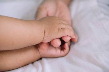 Bebeğin ve annenin ellerini beyaz yatak arka planında kapat.