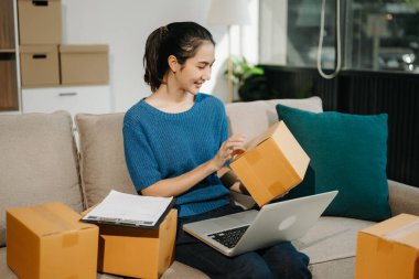 Genç Asyalı iş kadını, paket kutusu hazırla ve kanepedeki müşteriye teslimat için internetten siparişleri kontrol et. Çevrimiçi Alışveriş kavramı.