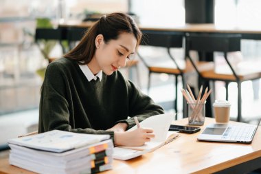 Başarılı Asyalı iş kadını ofiste çalışırken not defterine not alıyor.