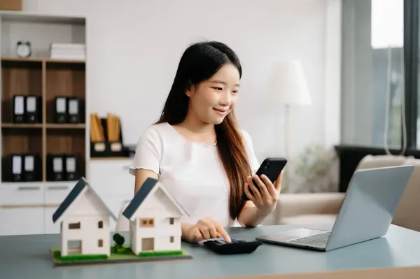 Young real estate agent worker working with laptop at table in modern office and small houses beside it