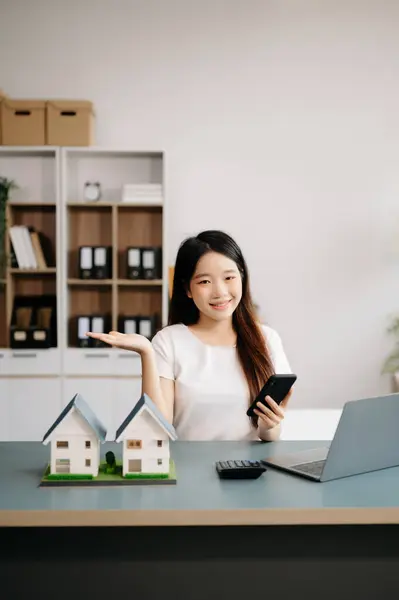 Young real estate agent worker working with laptop at table in modern office and small houses beside it