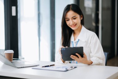 Ofiste çalışırken tablet kullanan genç Asyalı iş kadını.