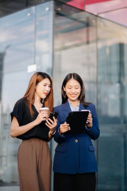 Şehirde dijital tablet kullanan ve kahve içen iki başarılı iş kadını.