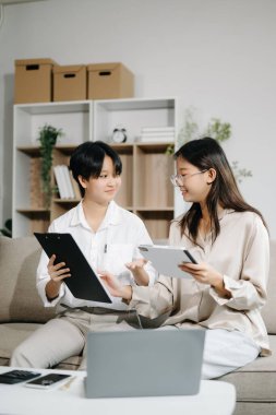 Ofisteki kanepede dizüstü bilgisayar ve tablet kullanan iki genç iş adamı.