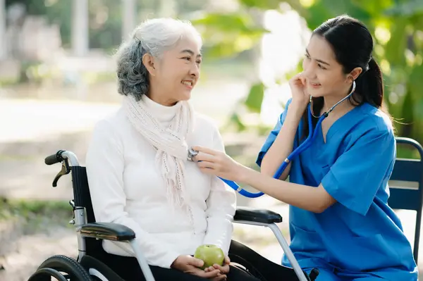 Elderly asian senior woman on wheelchair with careful caregiver in garden