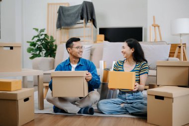 Büyük kutuları olan genç bir çift yeni bir eve taşınıyor. Asyalı erkek ve kadın, yeni ev ve taşınma konsepti için koltuğun üzerindeki kutuları kaldırmaya yardım ediyorlar. 