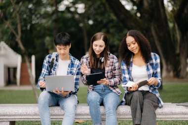 Öğrenciler kampüs parkını inceliyor. Gençler birlikte vakit geçiriyorlar. Tutma kitabı, dizüstü bilgisayar ve tablet 