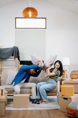 Büyük kutuları olan genç bir çift yeni bir eve taşınıyor. Asyalı erkek ve kadın, yeni ev ve taşınma konsepti için koltuğun üzerindeki kutuları kaldırmaya yardım ediyorlar. 