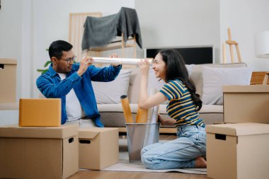 Büyük kutuları olan genç bir çift yeni bir eve taşınıyor. Asyalı erkek ve kadın, yeni ev ve taşınma konsepti için koltuğun üzerindeki kutuları kaldırmaya yardım ediyorlar. 