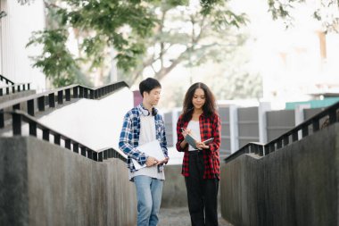 İki öğrenci kampüs parkını inceliyor. Gençler birlikte vakit geçiriyorlar. Kitap ve dizüstü bilgisayarı merdivenlerde tutmak 