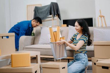 Büyük kutuları olan genç bir çift yeni bir eve taşınıyor. Asyalı erkek ve kadın, yeni ev ve taşınma konsepti için koltuğun üzerindeki kutuları kaldırmaya yardım ediyorlar. 