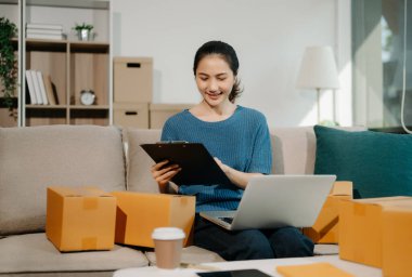 Başlangıçta küçük işletme KOBİ 'si, dizüstü bilgisayar kullanan girişimci kadın, paket ürün kutularını hazırlamak için çevrimiçi alışveriş siparişi alıyor ve kontrol ediyor