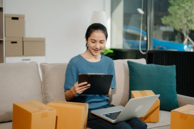 Başlangıçta küçük işletme KOBİ 'si, dizüstü bilgisayar kullanan girişimci kadın, paket ürün kutularını hazırlamak için çevrimiçi alışveriş siparişi alıyor ve kontrol ediyor