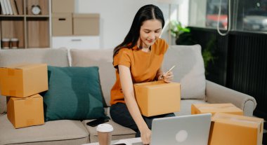 Başlangıçta küçük işletme KOBİ 'si, dizüstü bilgisayar kullanan girişimci kadın, paket ürün kutularını hazırlamak için çevrimiçi alışveriş siparişi alıyor ve kontrol ediyor