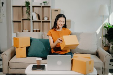 Küçük işletme girişimcisi KOBİ 'li kadın ev ofisinde kutu, dizüstü bilgisayar, tablet bilgisayar ve kahveyle çalışıyor