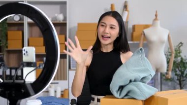 Küçük işletme girişimcisi KOBİ serbest. Ev ofisinde çalışan Asyalı bir kadın sosyal medya için paketleme ve akıllı telefon ve yüzük lambası kullanıyor.